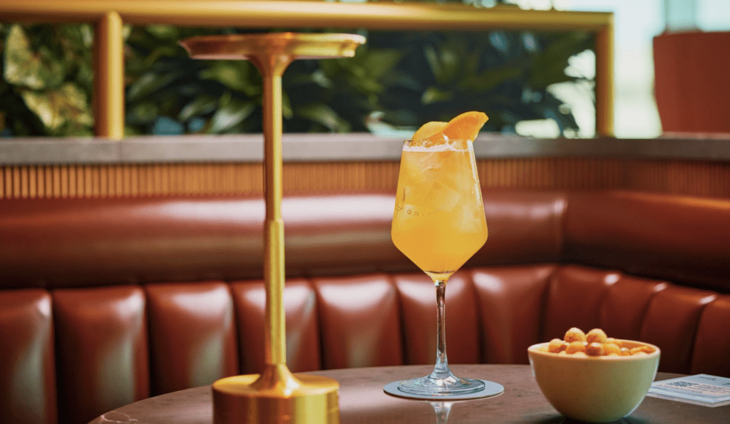 a glass of orange liquid with a slice of orange on top of a table